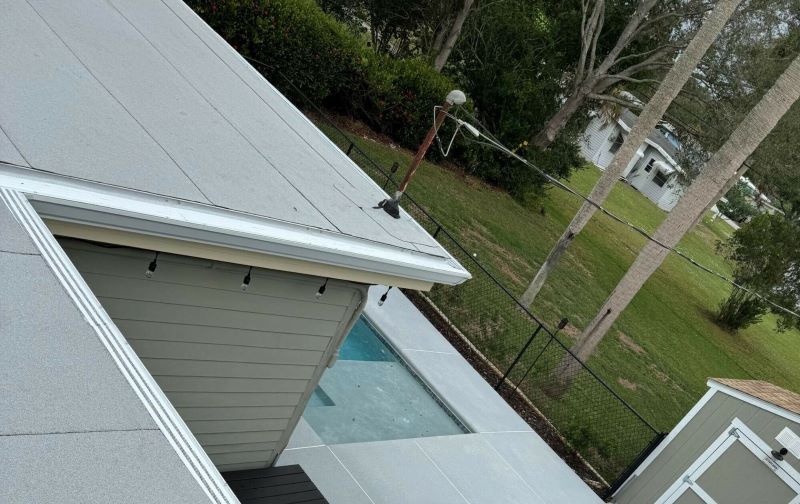A view from a rooftop shows a backyard with a swimming pool, surrounded by a grass lawn and trees. There is a detached shed near the pool and some outdoor lighting along the roofline. The background includes a fence and more trees, creating an inviting atmosphere that’s ideally free of any termite infestation.