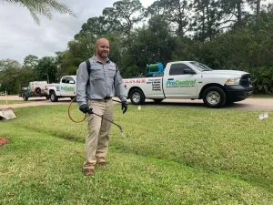 Man sprays lawn treatment on green grass while ProControl service trucks are parked along the street in the background