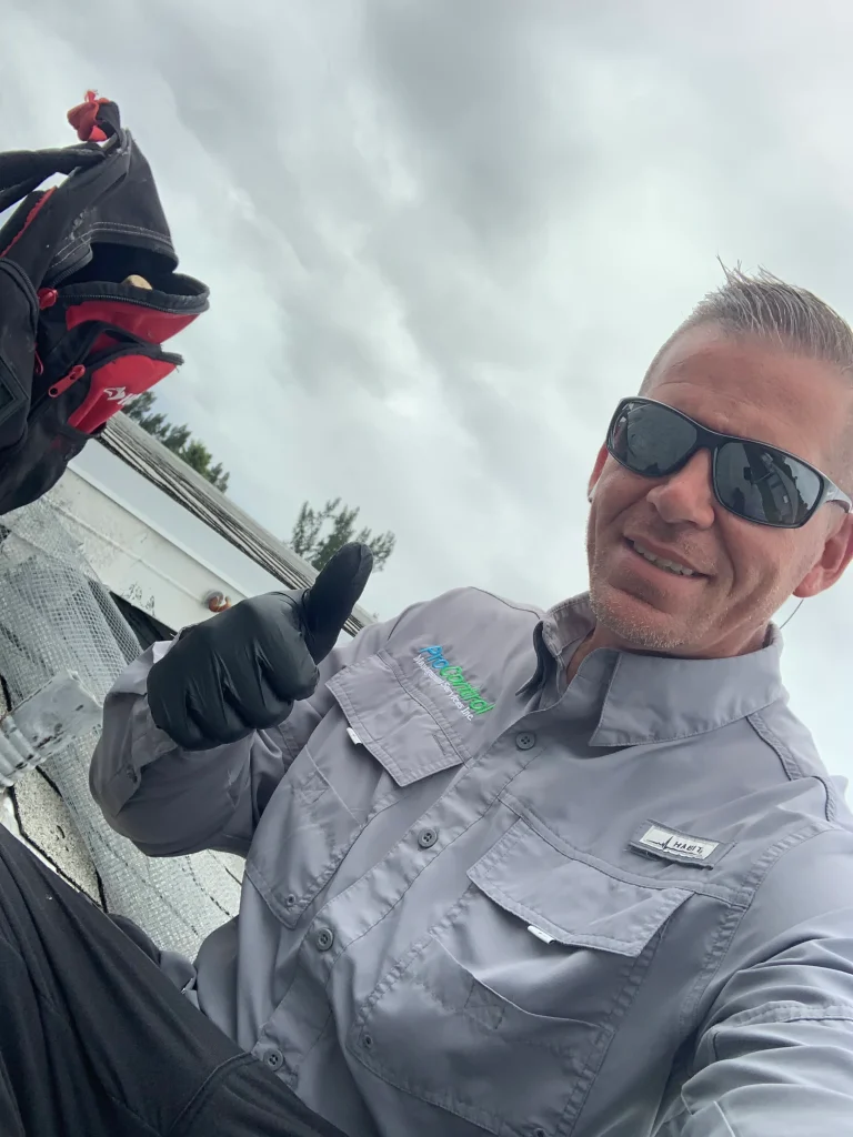 A man wearing sunglasses and gloves gives a thumbs up on a rooftop beneath a cloudy sky.