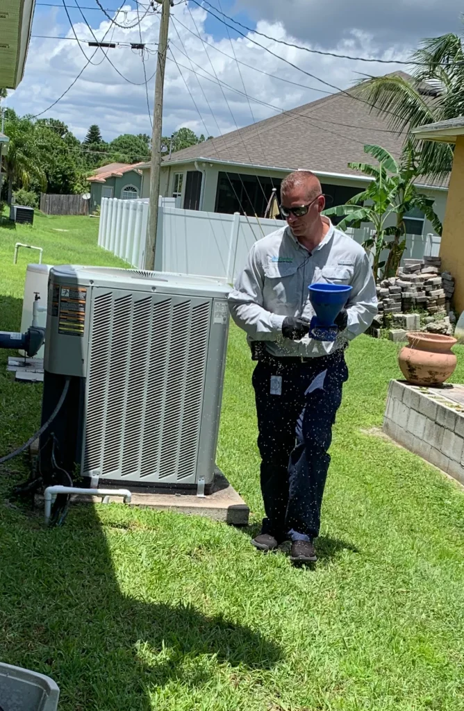 An HVAC technician wearing sunglasses and gloves checks an outdoor AC unit with a blue funnel on a sunny day.